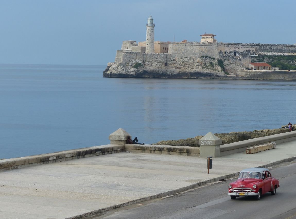 Un coche clásico en La Habana pasa frente al Castillo del Morro, un símbolo histórico de la ciudad.
