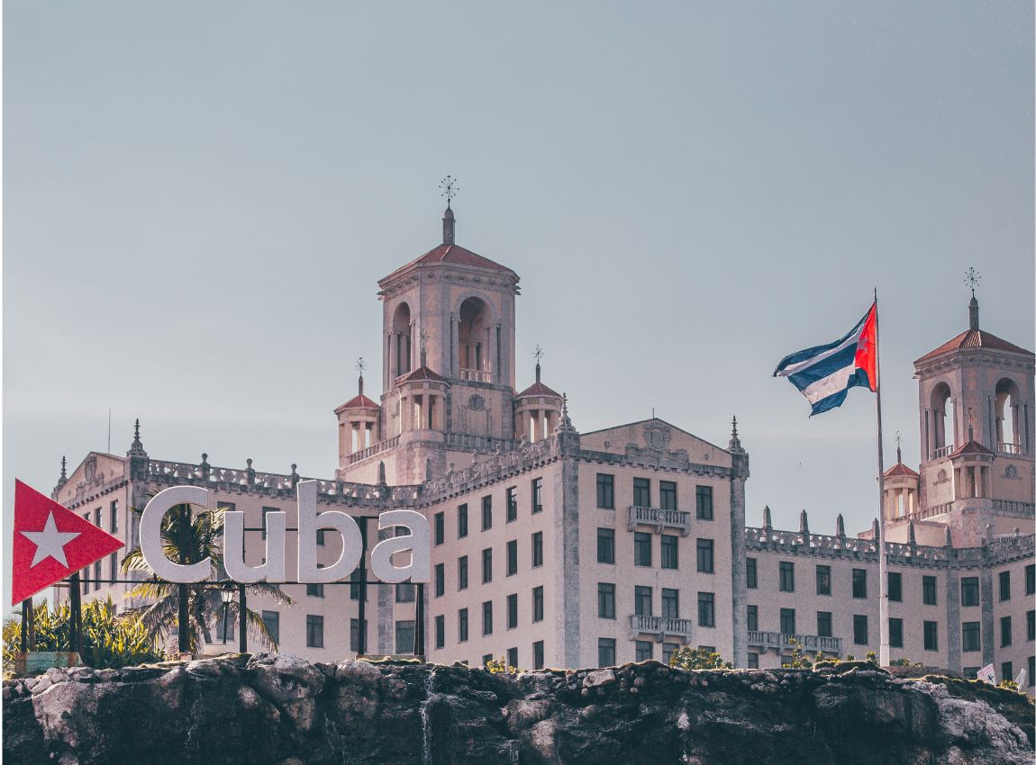 Vista del Hotel en La Habana, con su arquitectura distintiva y el letrero "Cuba". Una bandera cubana ondea a la derecha del edificio, y otra a la izquierda.